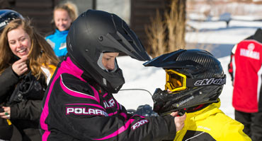 Mother adjusting helmet strap on young snowmobiler