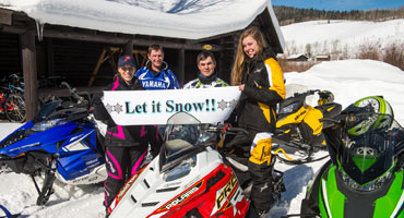 Snownobilers holding sign that says Let it Snow